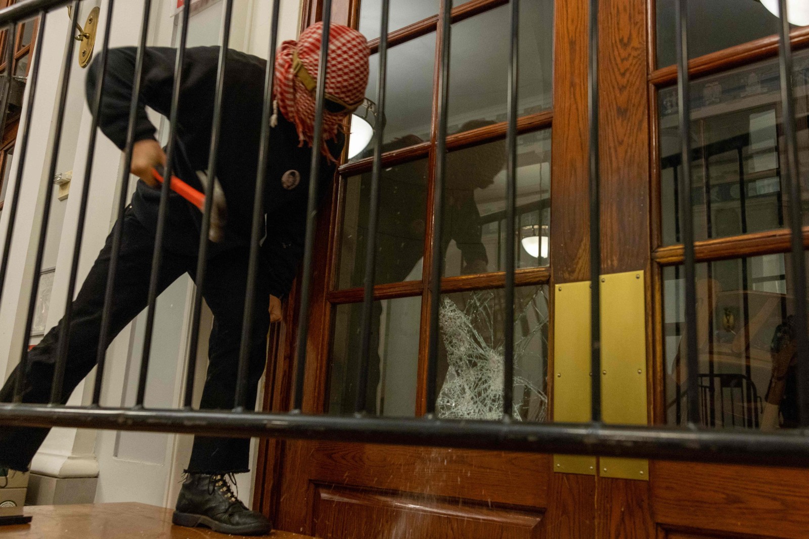 Um manifestante quebra as janelas da porta da frente do prédio para prender uma corrente em torno dele para impedir a entrada das autoridades na terça-feira, 30 de abril de 2024, na cidade de Nova York. — Foto: Alex Kent/Getty Images/AFP