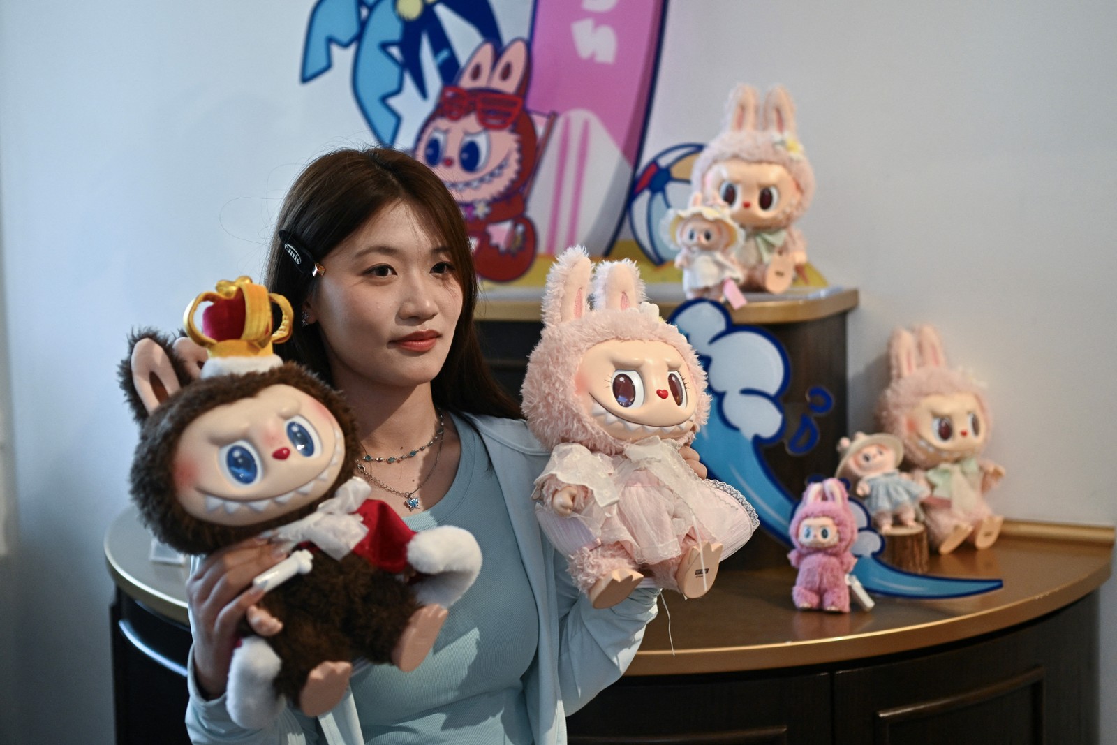 Mulher posando com os personagens Labubu (E) e Mokoko em um salão de exposições enquanto visita o parque temático Pop Land da Pop Mart, em Pequim — Foto: PEDRO PARDO / AFP
