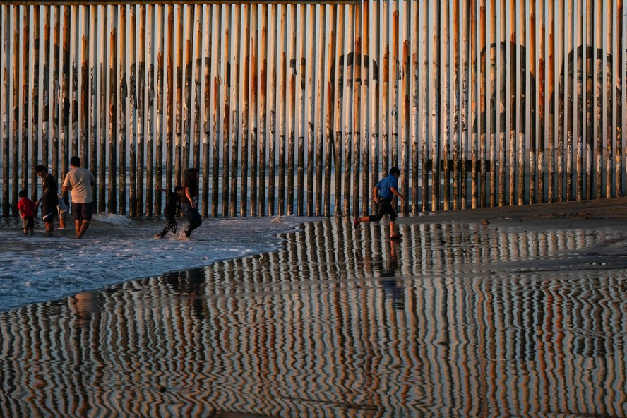 Pessoas caminham em Tijuana, no México, ao lado do muro na fronteira com os EUA