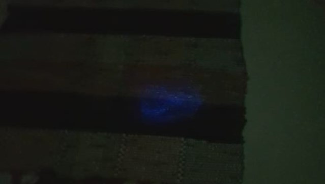 Visão do tapete, após aplicação do Luminol, revelando a mancha circular — Foto: Reprodução