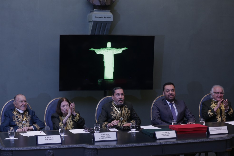 Acadêmicos reunidos, com o presidente da ABL, Merval Pereira, ao centro, e a imagem do Cristo iluminado de verde em homenagem aos 125 anos da instituição — Foto: Alexandre Cassiano
