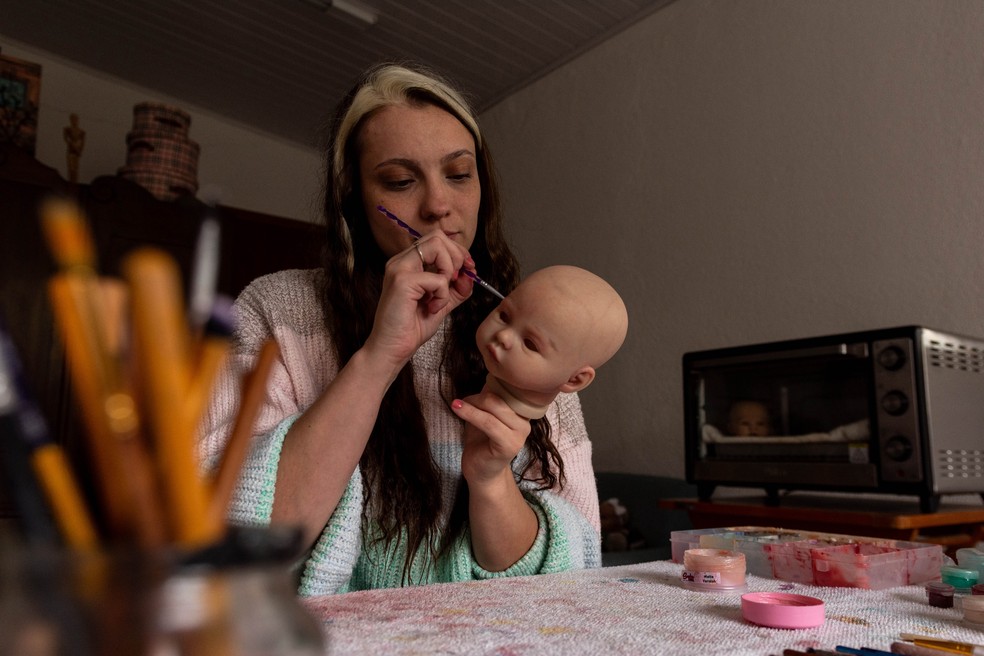 Vivi Louhrinci, atriz e artista que cria bonecas reborn desde 2020, pinta delicadamente uma boneca em Curitiba, Brasil, em 6 de junho de 2025 — Foto: The New York Times
