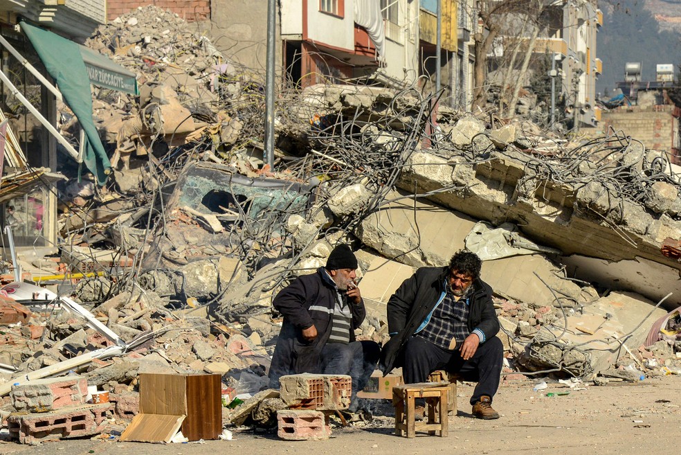 Parentes das vítimas sentam-se ao lado dos escombros de um prédio que desabou em Adiyaman após o terremoto que atingiu o Sudeste da Turquia — Foto: Ilyas Akengin/AFP